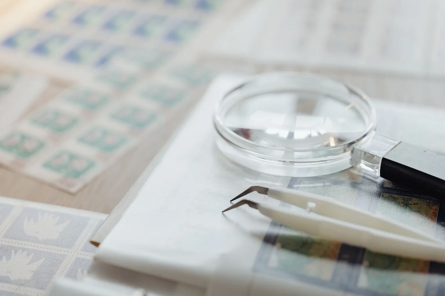 Magnifying glass and stamp tongs beside album pages