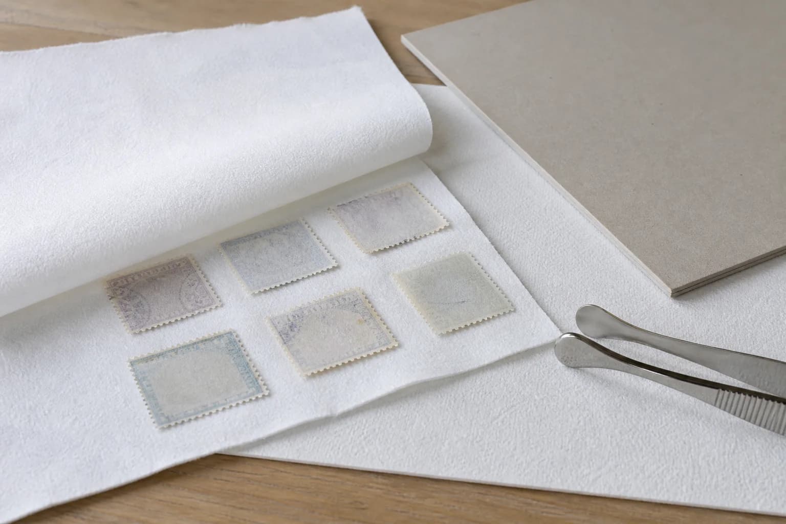 Fictional soaked stamps placed face down on clean white blotting paper with a cover sheet, flat archival board and stamp tongs