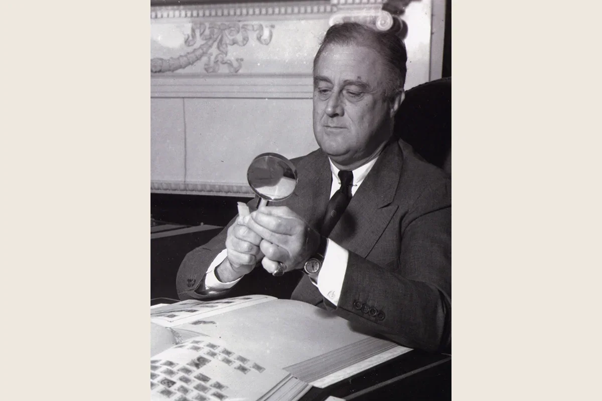 Historical black-and-white photograph of Franklin D. Roosevelt examining his stamp collection