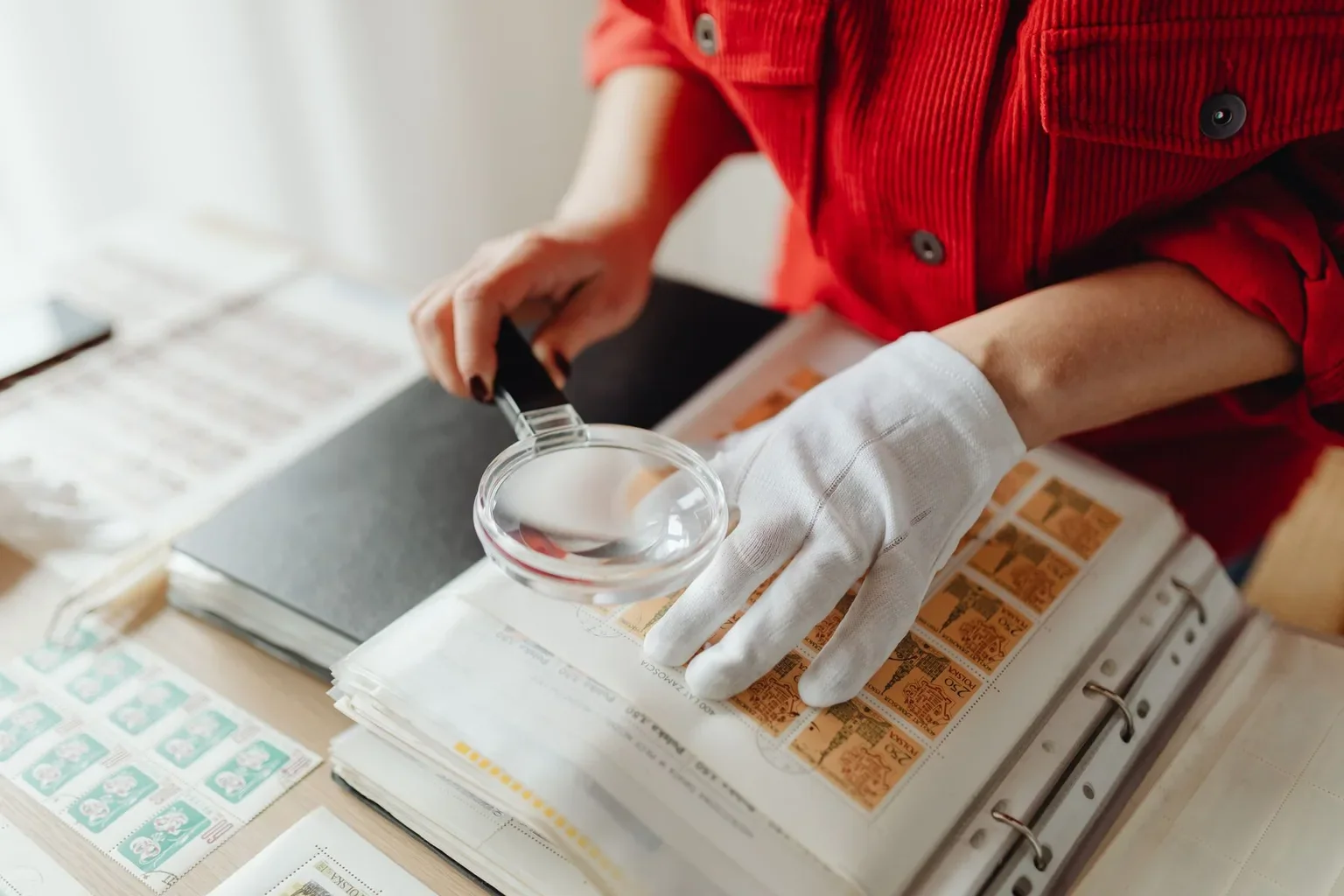 Gloved collector examining stamps in an open album with a magnifying glass